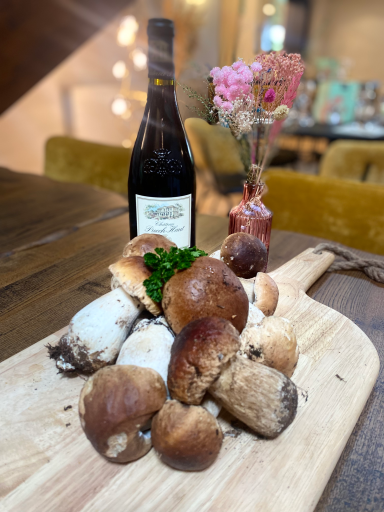 Champignons variés sur une planche en bois, avec une bouteille de vin et des fleurs en arrière-plan.